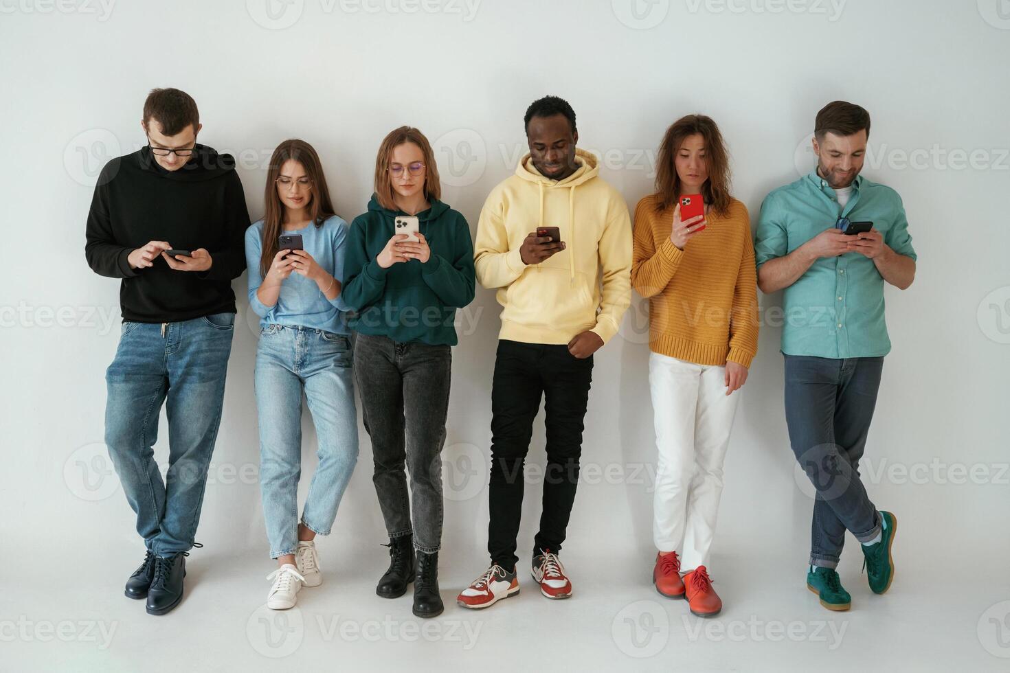 Busy by using ,,smartphones. Group of young people are standing against white background photo