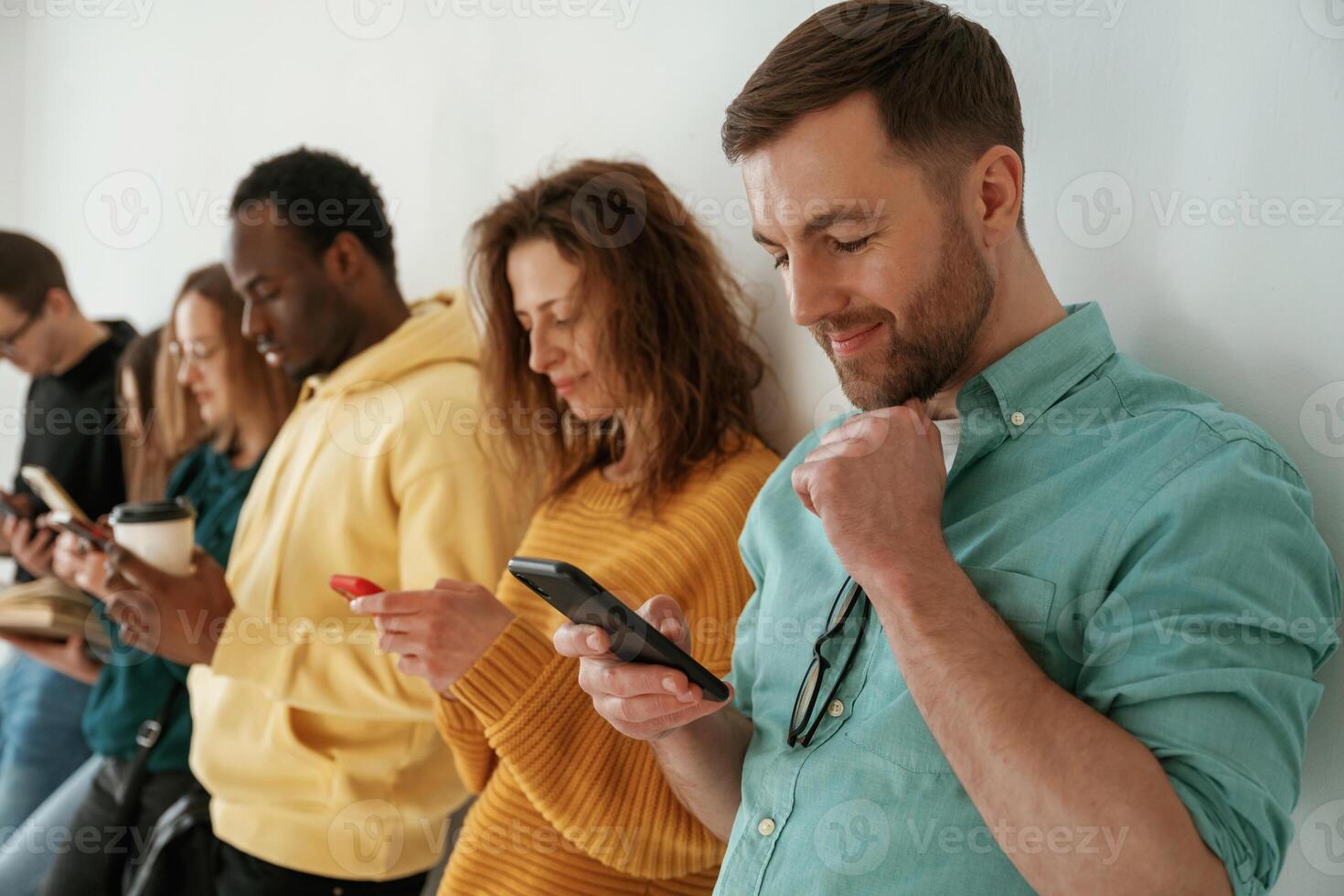 Busy by using, smartphones. Group of young people are standing against white background photo