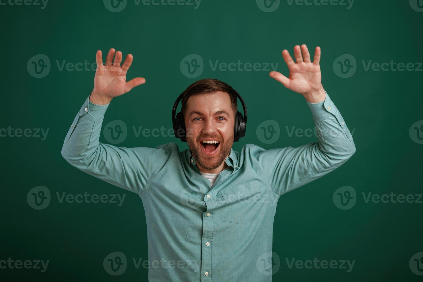 With hands up, in headphones. Man is standing against background in the studio photo