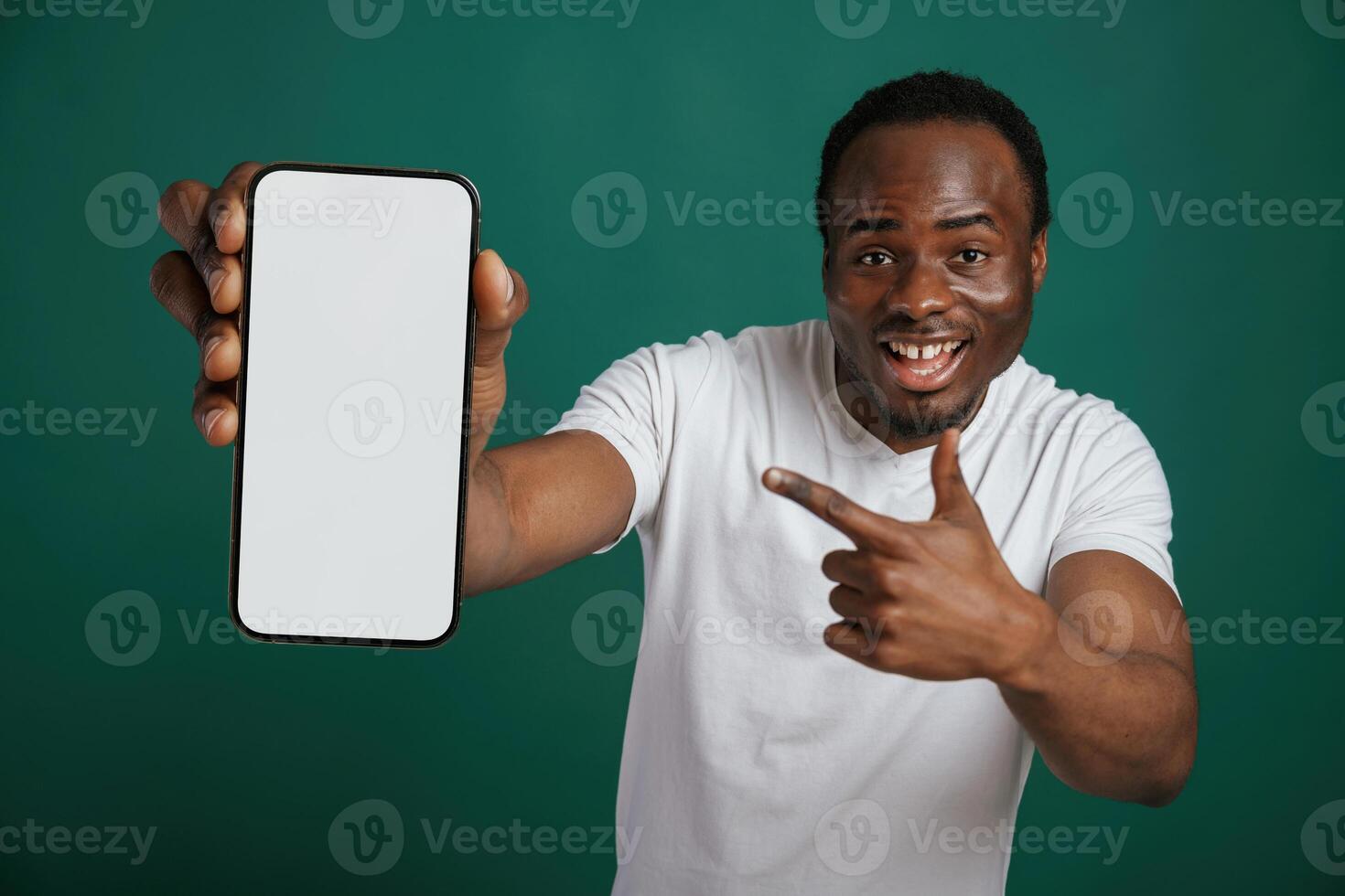 Smartphone with, white empty space for text. African American man is standing against green background in the studio photo