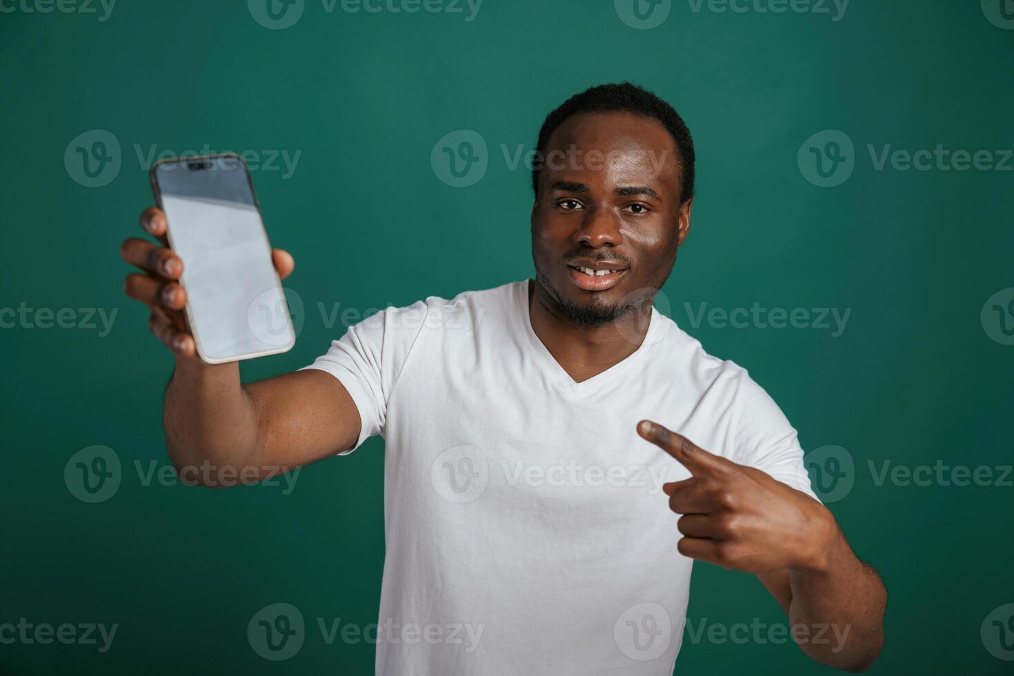 Smartphone with white ,empty space for text. African American man is standing against green background in the studio photo