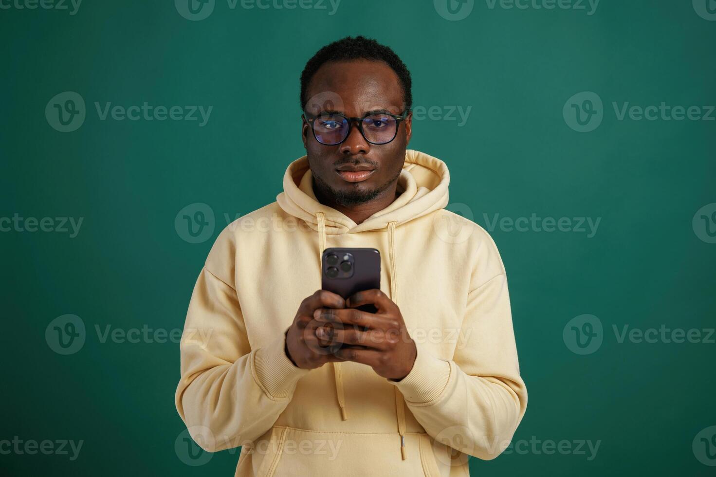 Using smartphone.. African ,American man is standing against green background in the studio photo