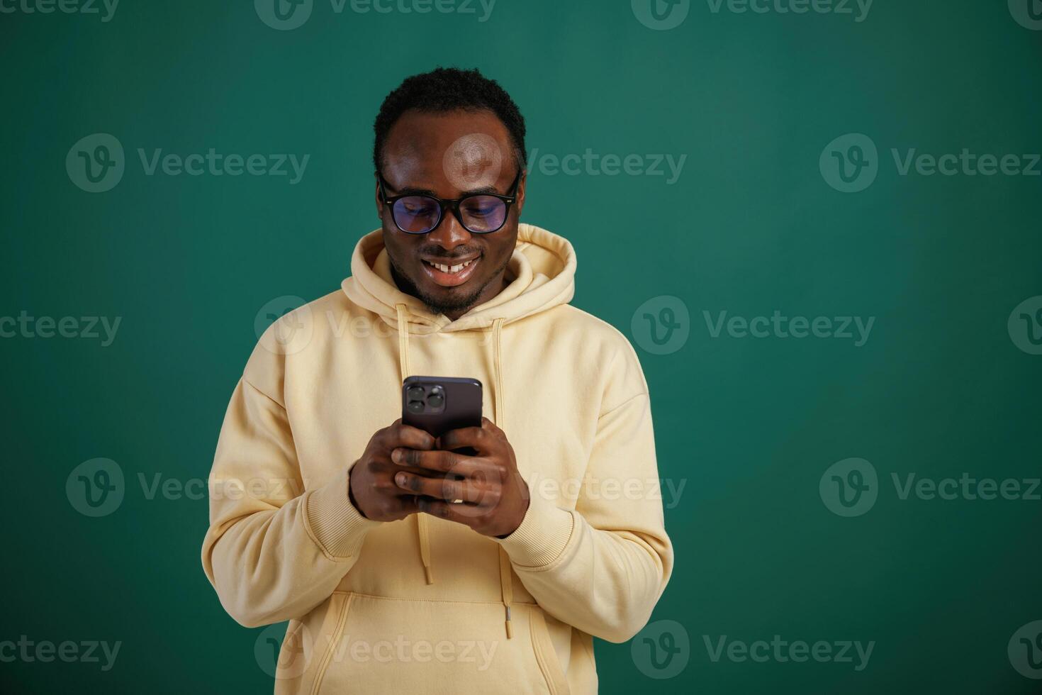 Using ,smartphone. African American man is standing against green background in the studio photo