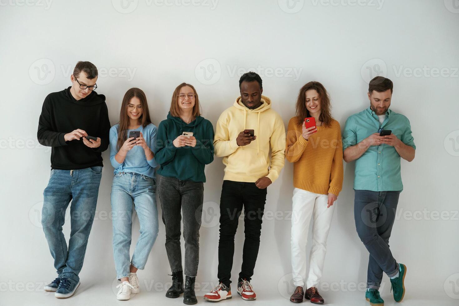 Joyful, holding,, smartphones. Group of young people are standing against white background photo