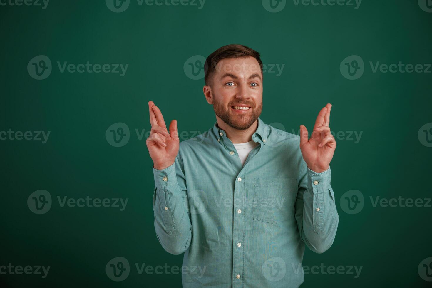 Fingers crossed, hoping for better. Man is standing against background in the studio photo