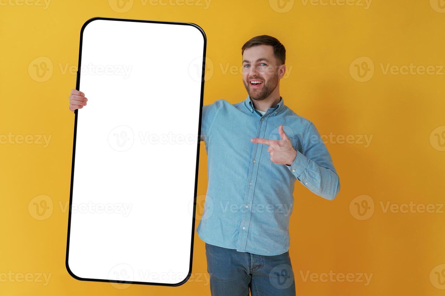 Big smartphone, place ,for copy space. Attractive man in blue shirt is against yellow background photo