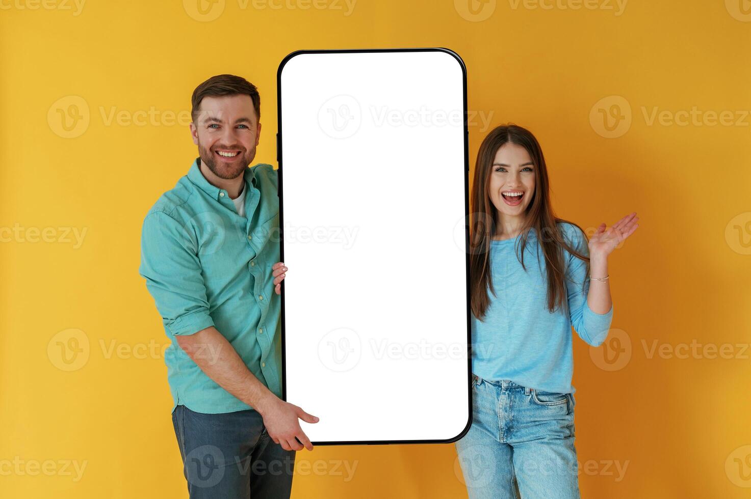 Holding white display ,of smartphone, copy space. Man and woman are standing against yellow background photo