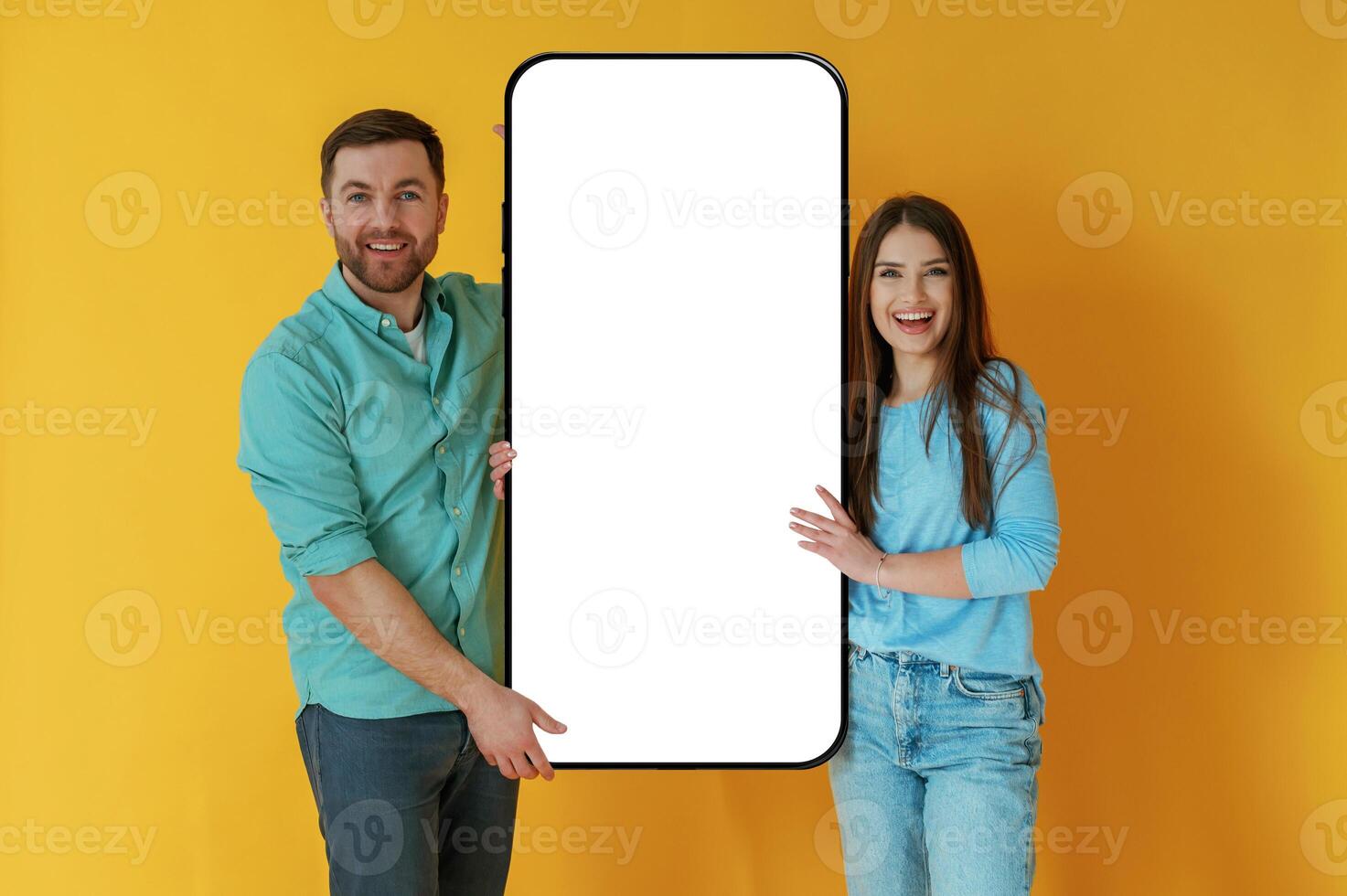 Display for copy space. Man and woman are standing with large smartphone against yellow background photo