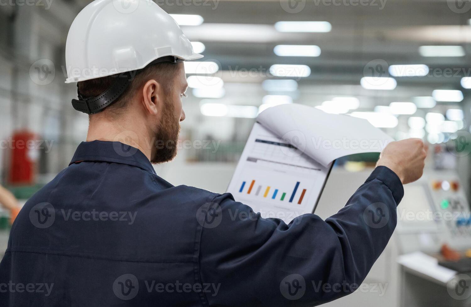 Turning the pages of documents,. Factory worker is indoors with hard hat photo