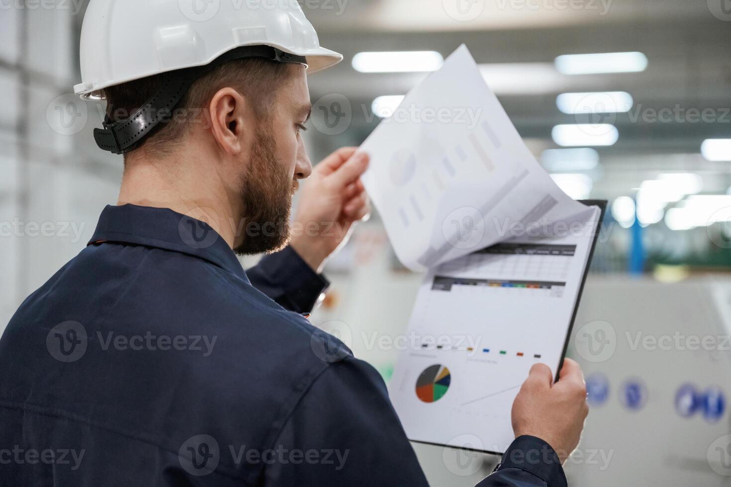 Turning the pages of documents... Factory worker is indoors with hard hat photo