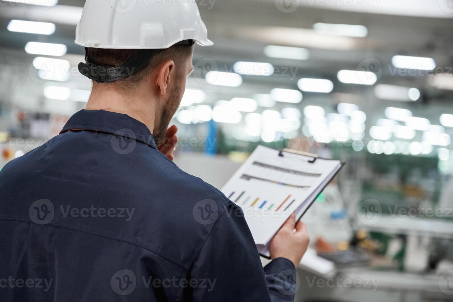 Back view, with notepad and graphs. Factory worker is indoors with hard hat photo