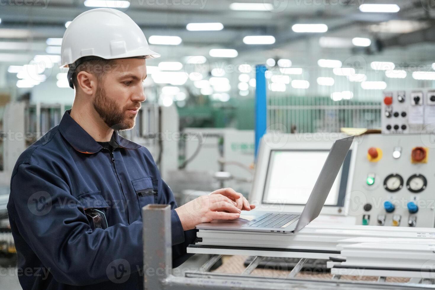Using,, the laptop. Factory, worker is indoors with hard hat photo