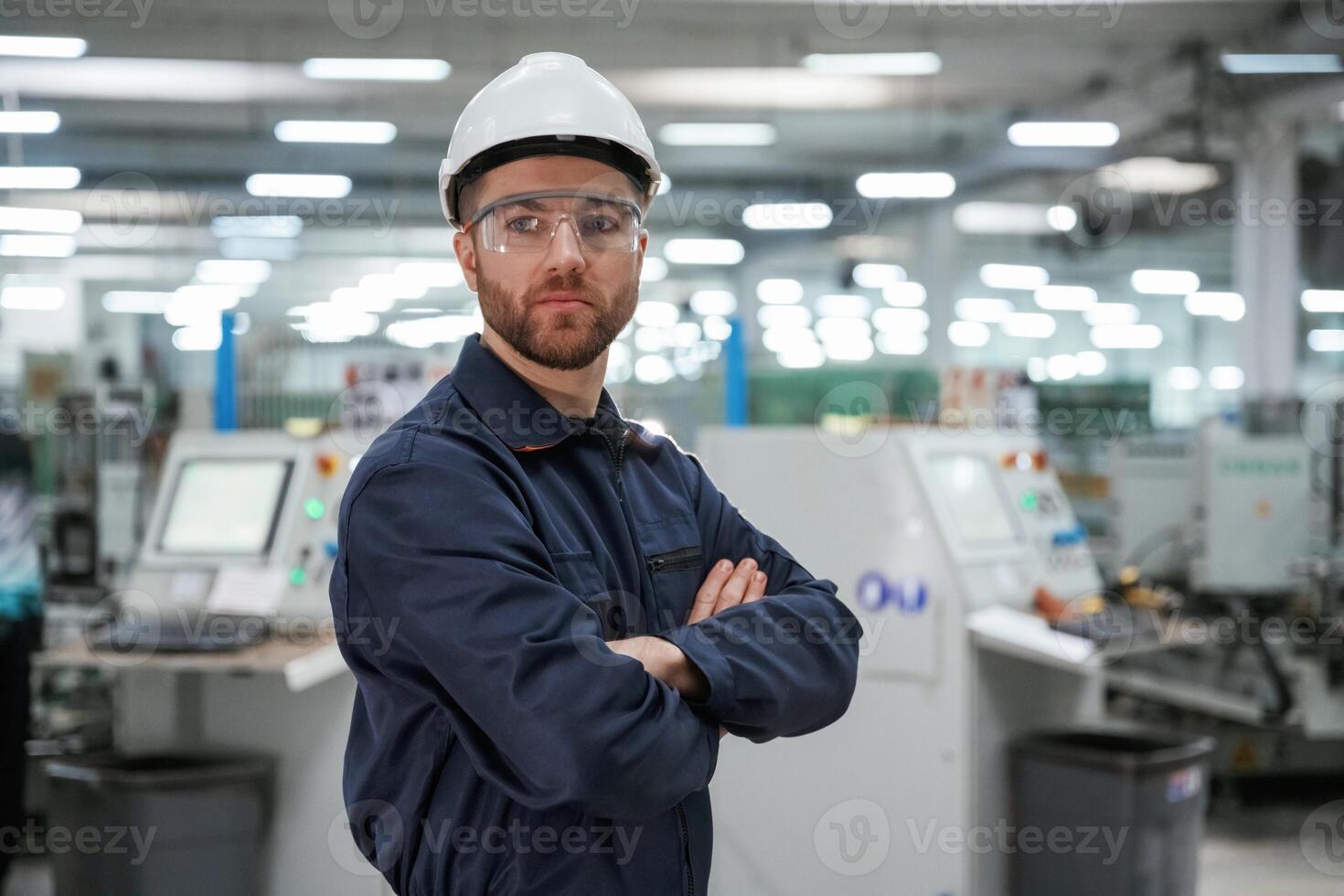 Posing, with,, arms ,crossed. Factory worker is indoors with hard hat photo