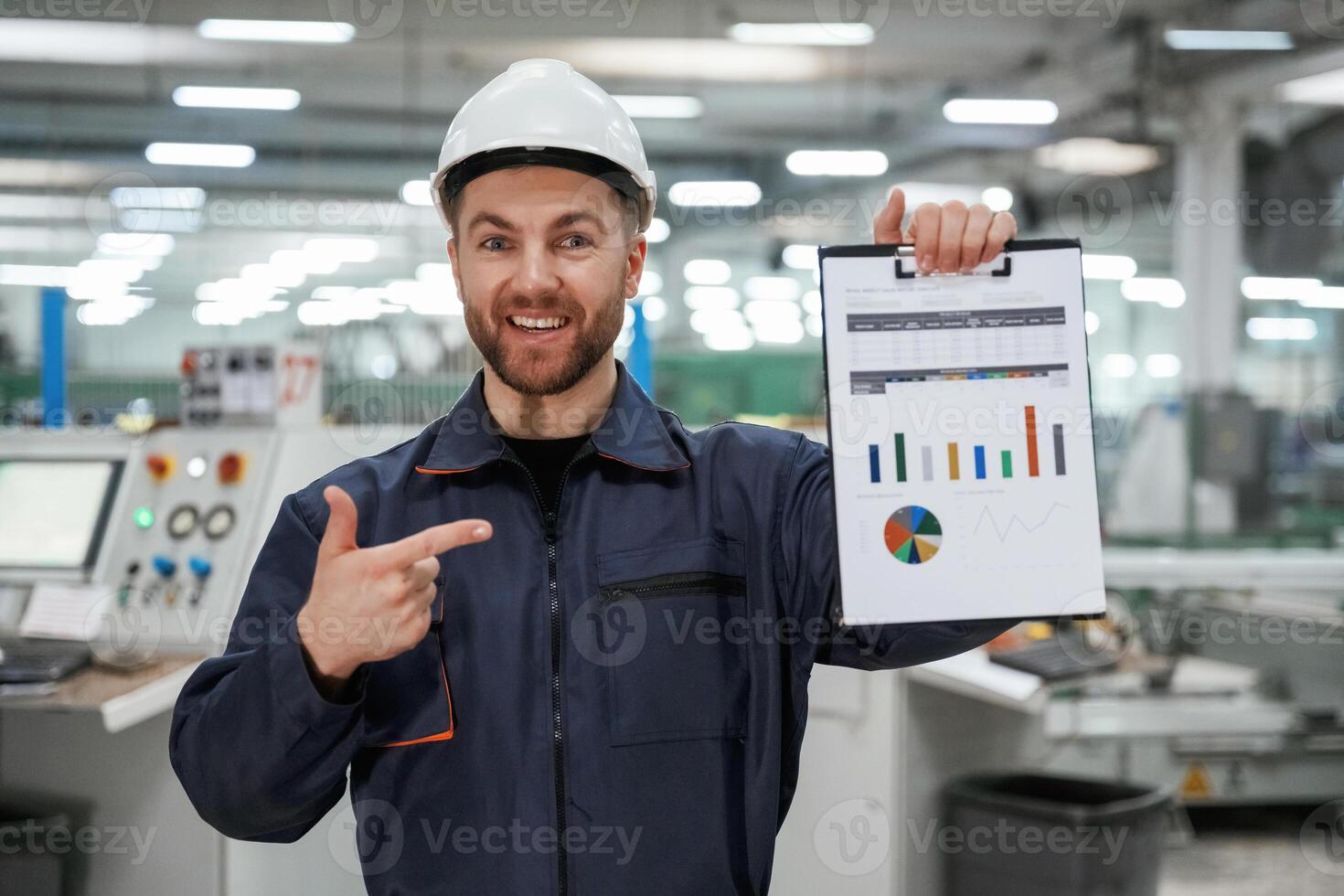 Plan, with ,graphs in hand. Factory worker is indoors with hard hat photo