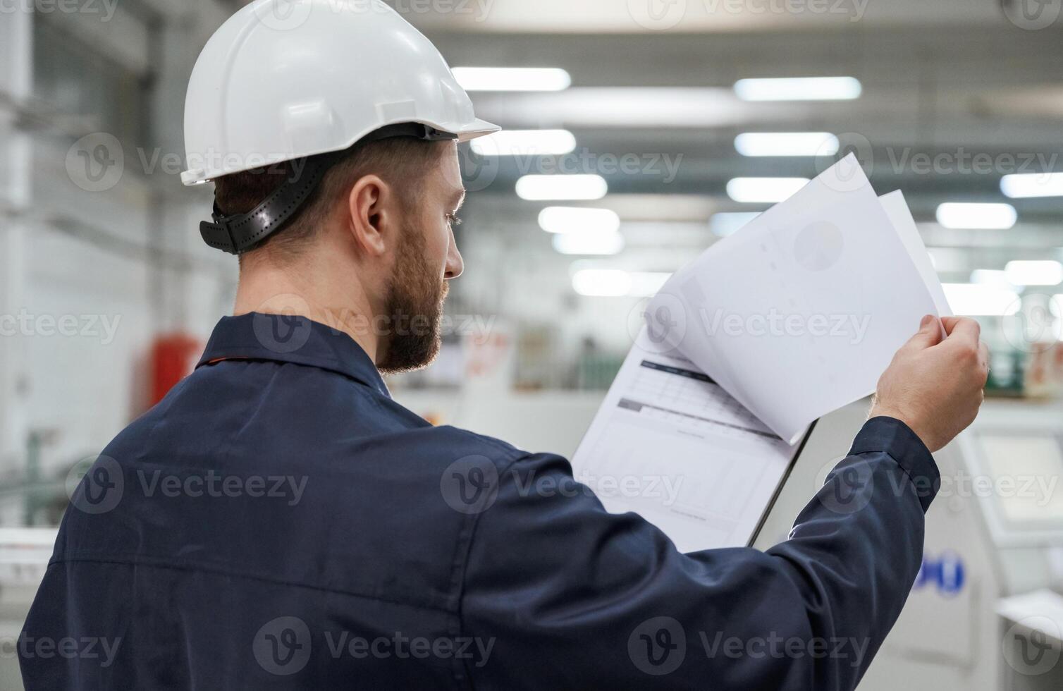 Turning, the pages of documents.. Factory worker is indoors with hard hat photo