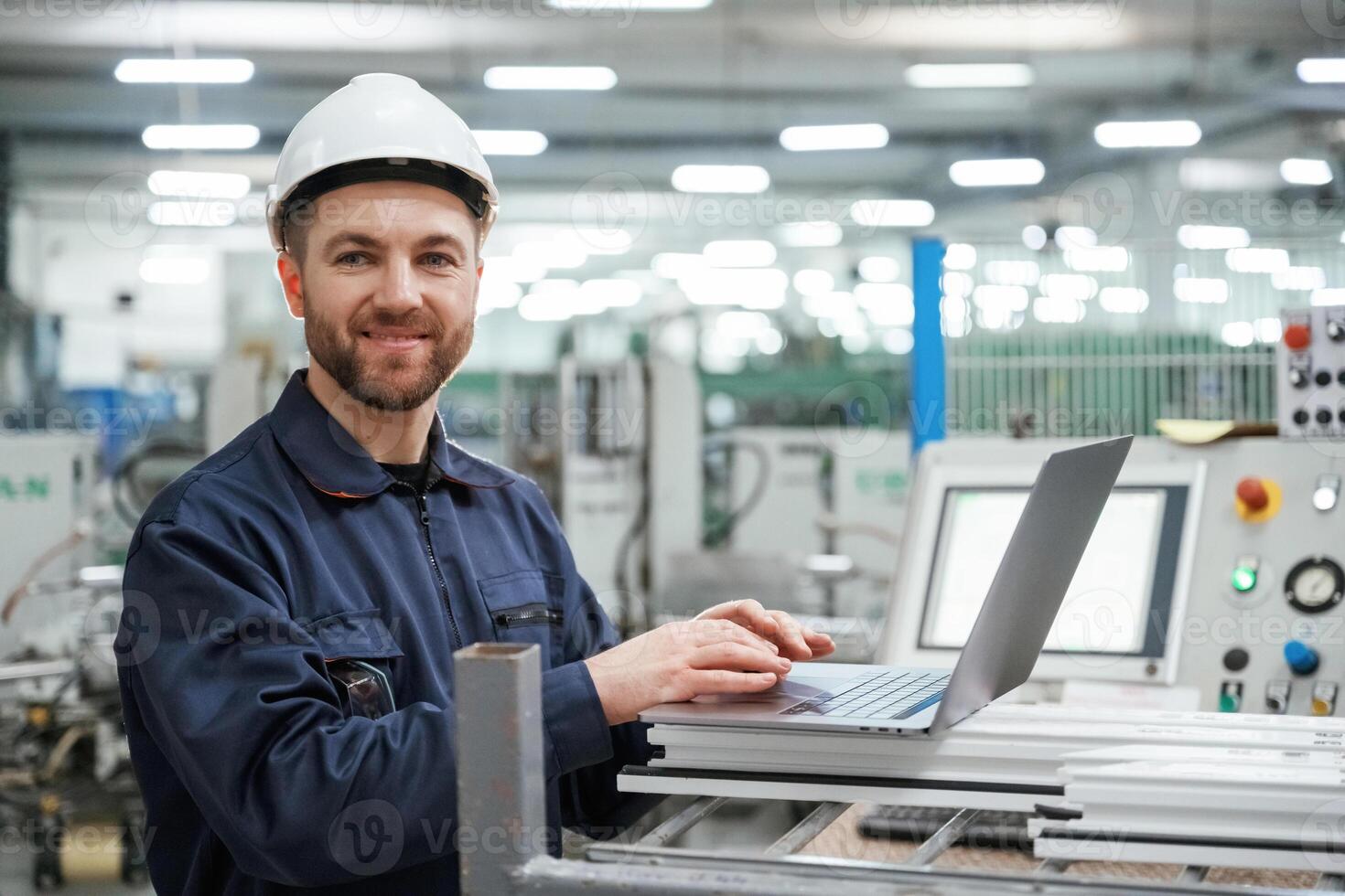 Using the laptop., Factory worker is indoors with hard hat photo