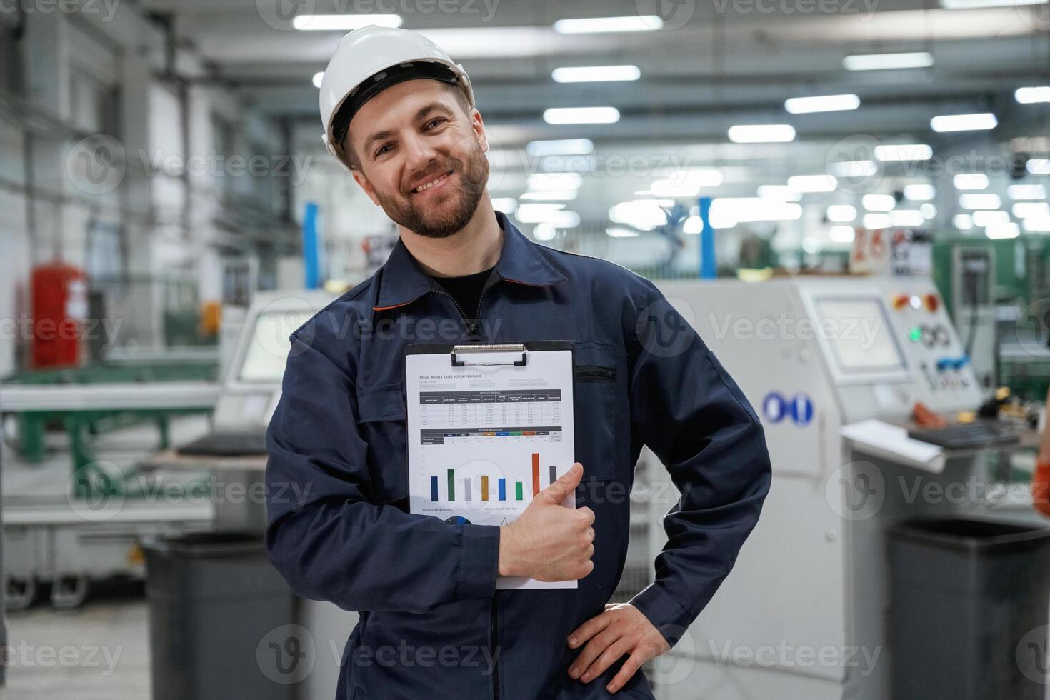 Happy, with ,results, holding graphs. Factory worker is indoors with hard hat photo