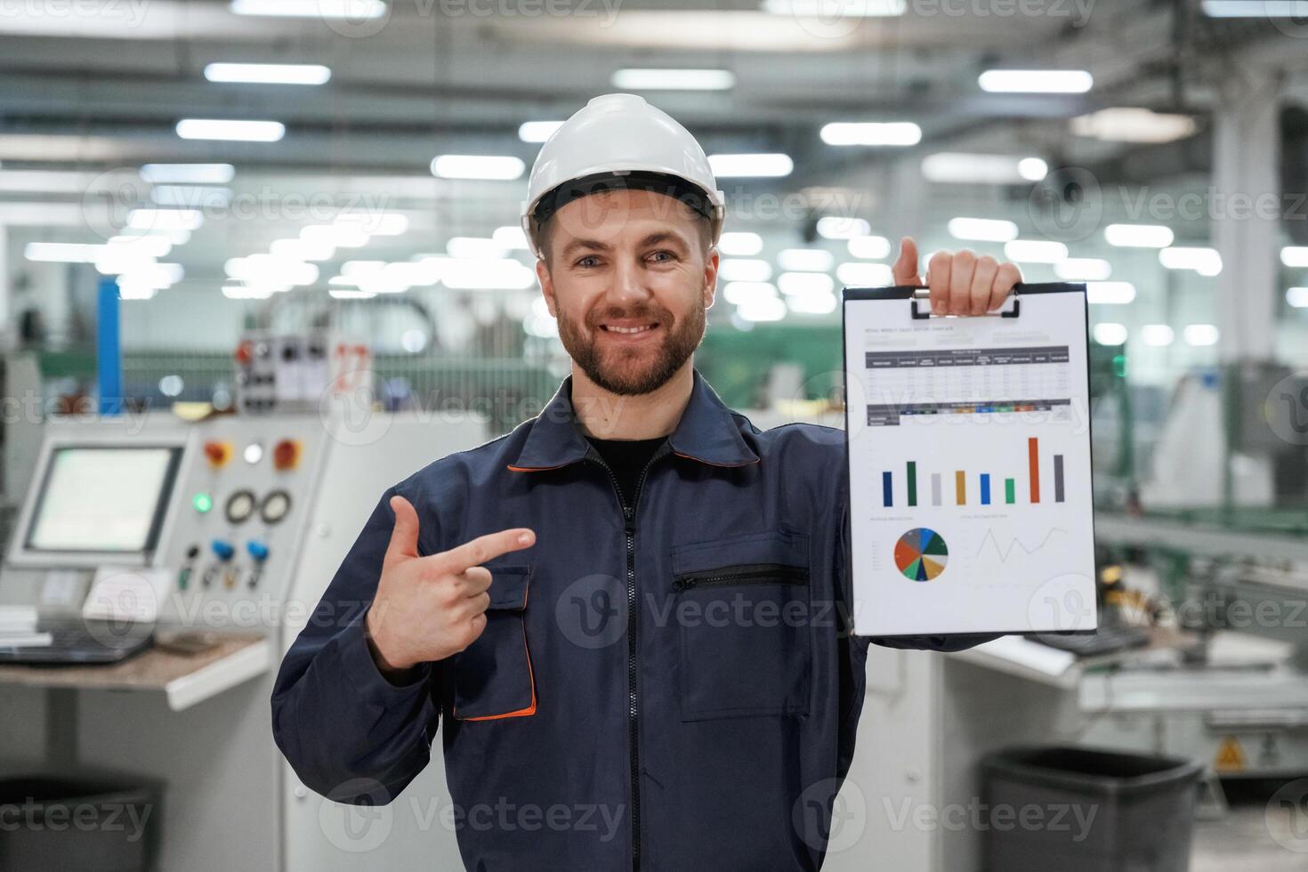 Plan with ,graphs ,,in hand. Factory worker is indoors with hard hat photo