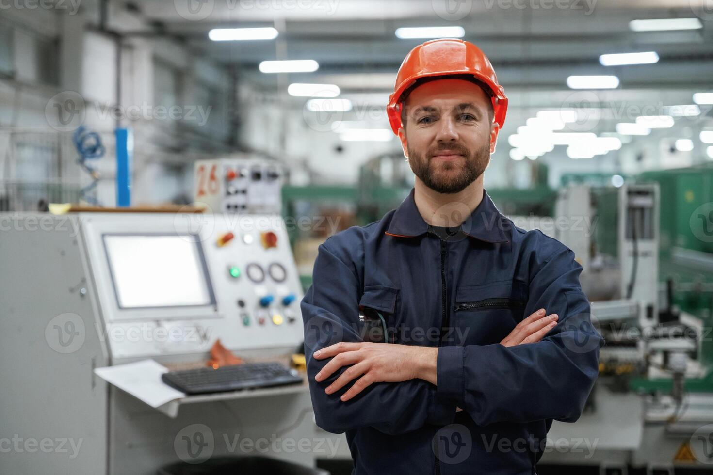Standing, with arms crossed. Factory,, worker is indoors with hard hat photo