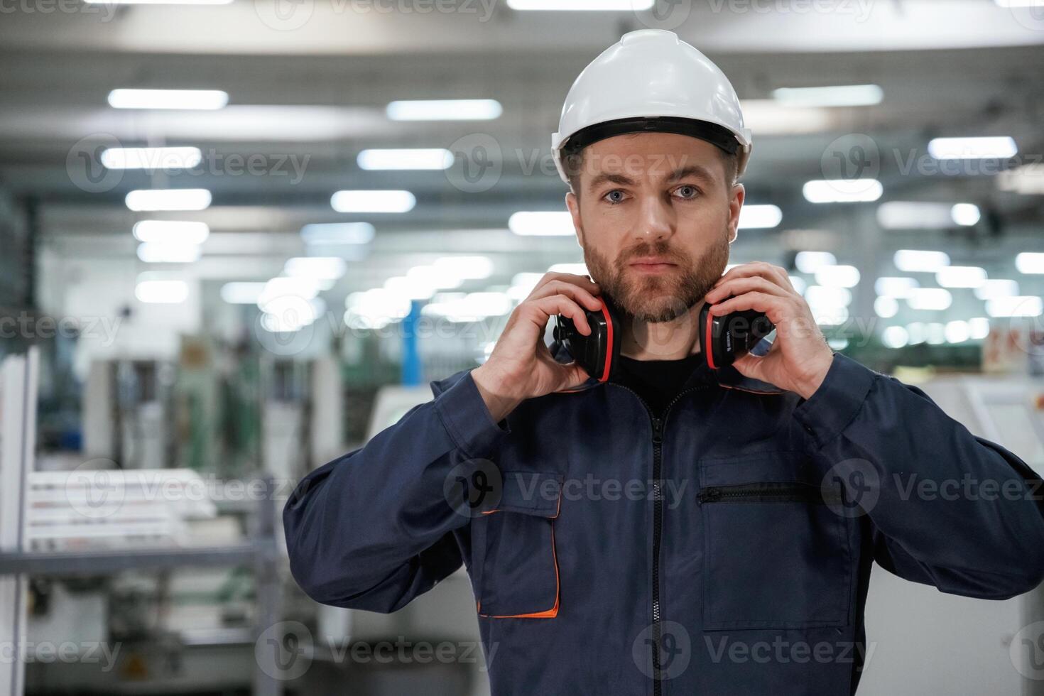 With ,protective, headphones. Factory worker is indoors with hard hat photo