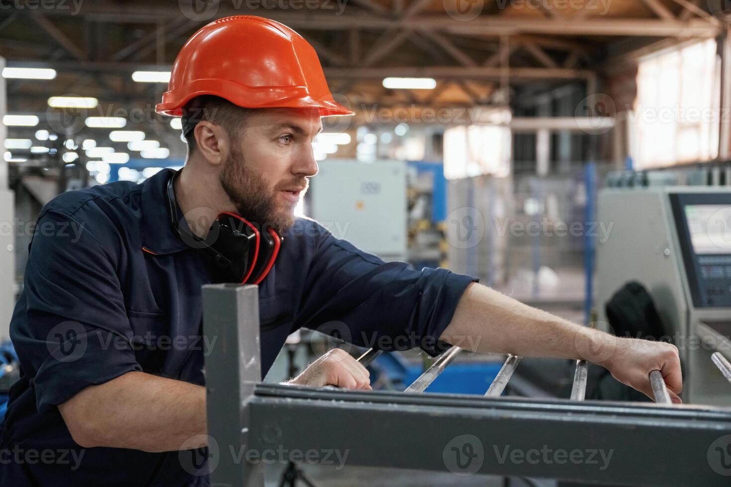 Working with machinery. Factory worker is indoors with hard hat photo