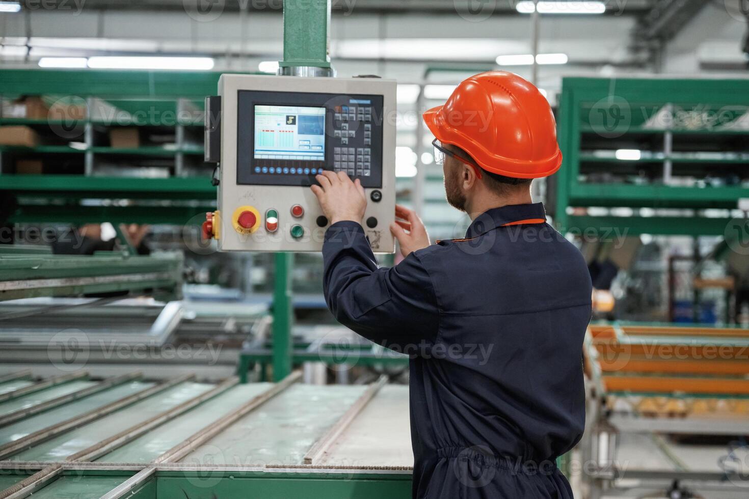 Adjusting settings of,machine, operating. Factory worker is indoors with hard hat photo