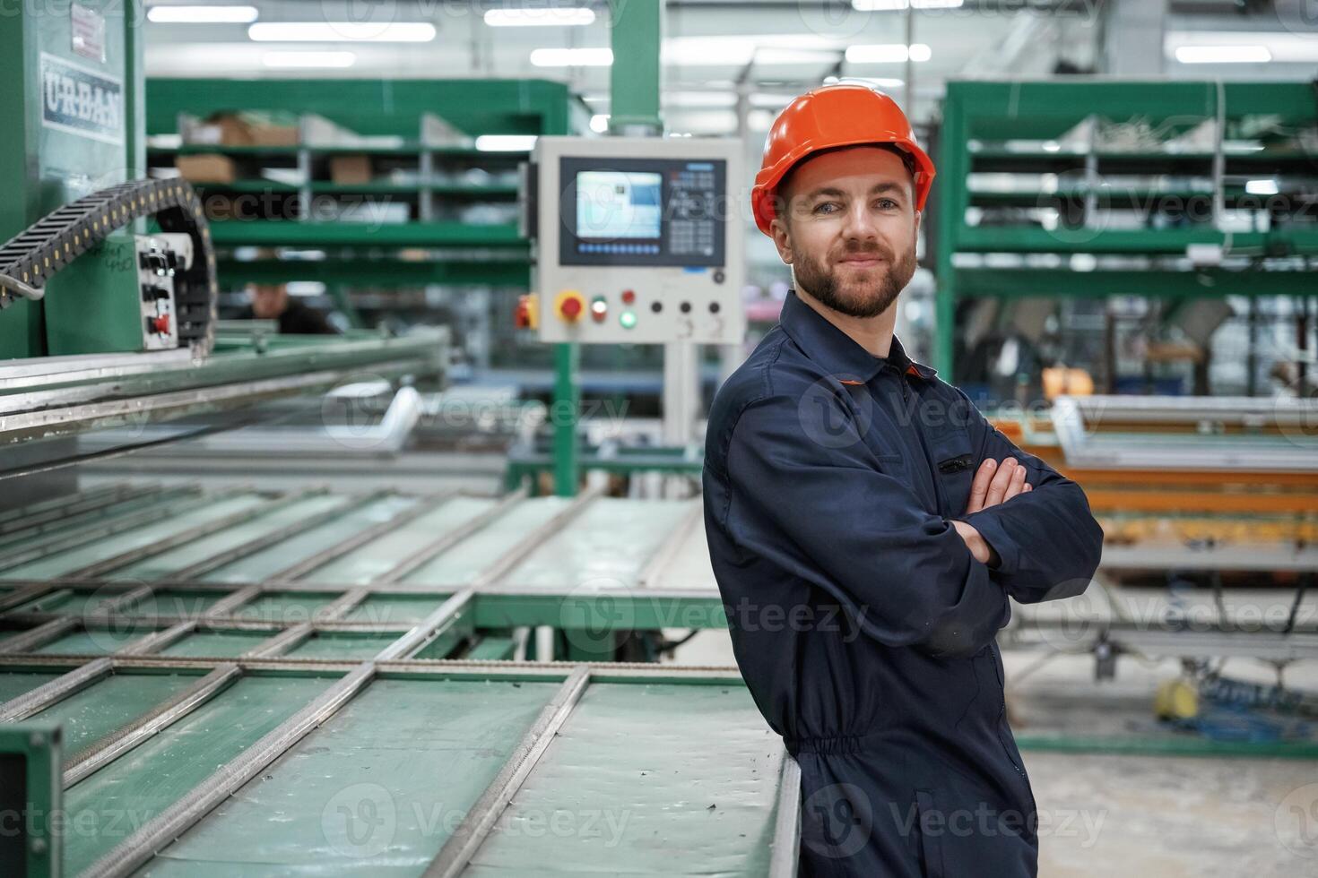 Beautiful man, is standing with arms crossed. Factory worker is indoors with hard hat photo
