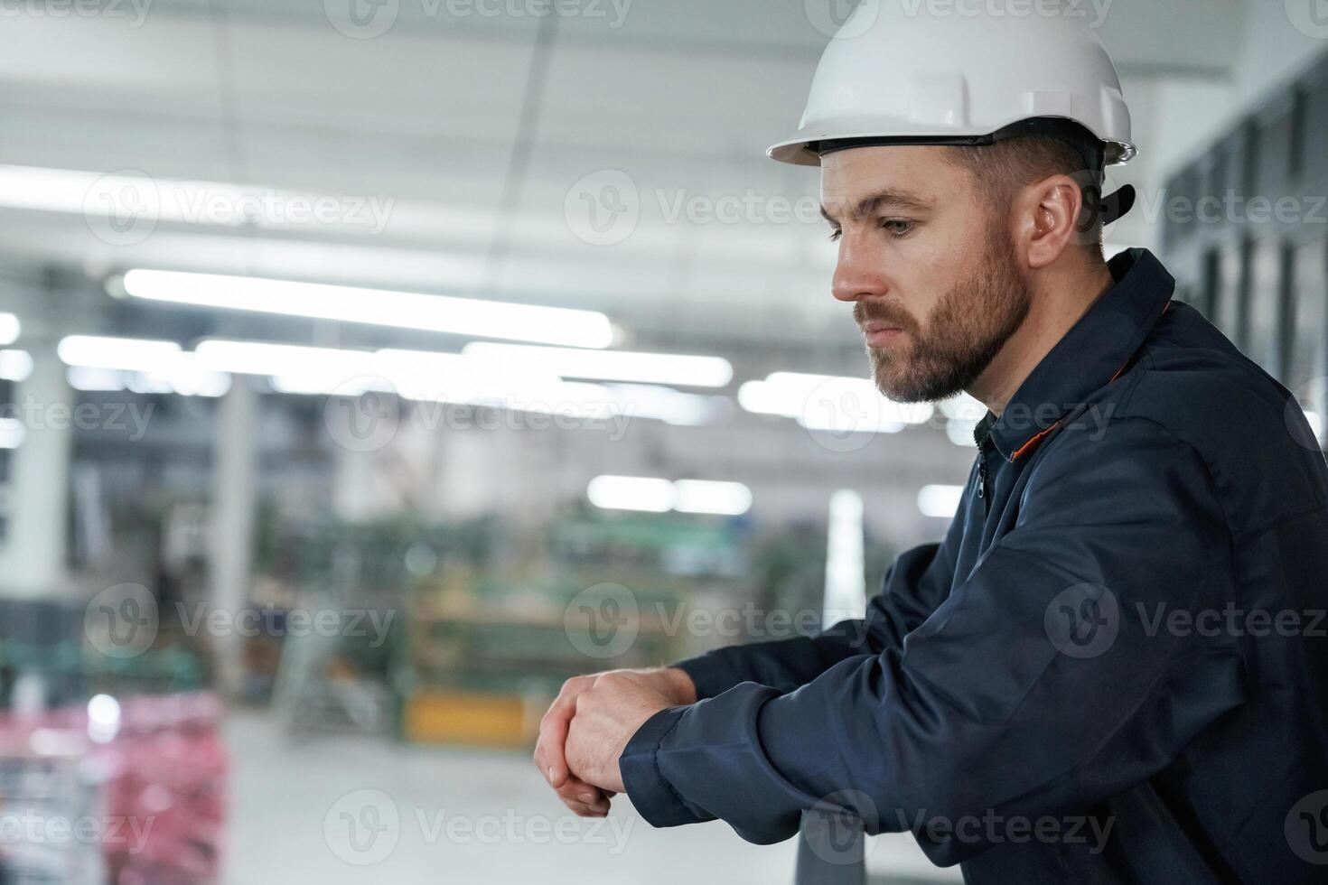 Leaning on the, railings. Factory worker is indoors with hard hat photo