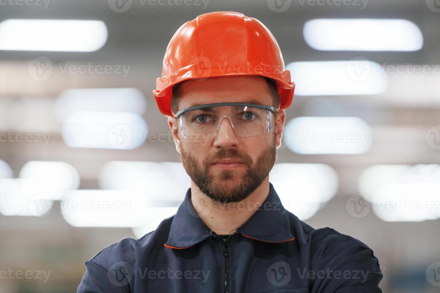 Focused, portrait, in glasses. Factory worker is indoors with hard hat photo