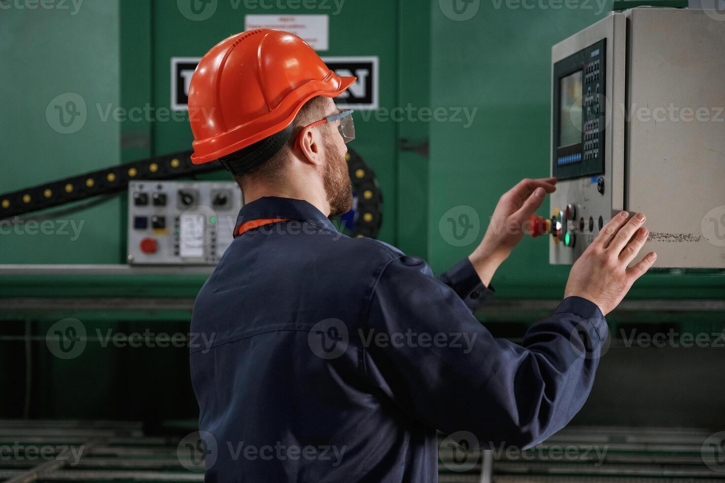 Green, colored machine, operator is busy. Factory worker is indoors with hard hat photo