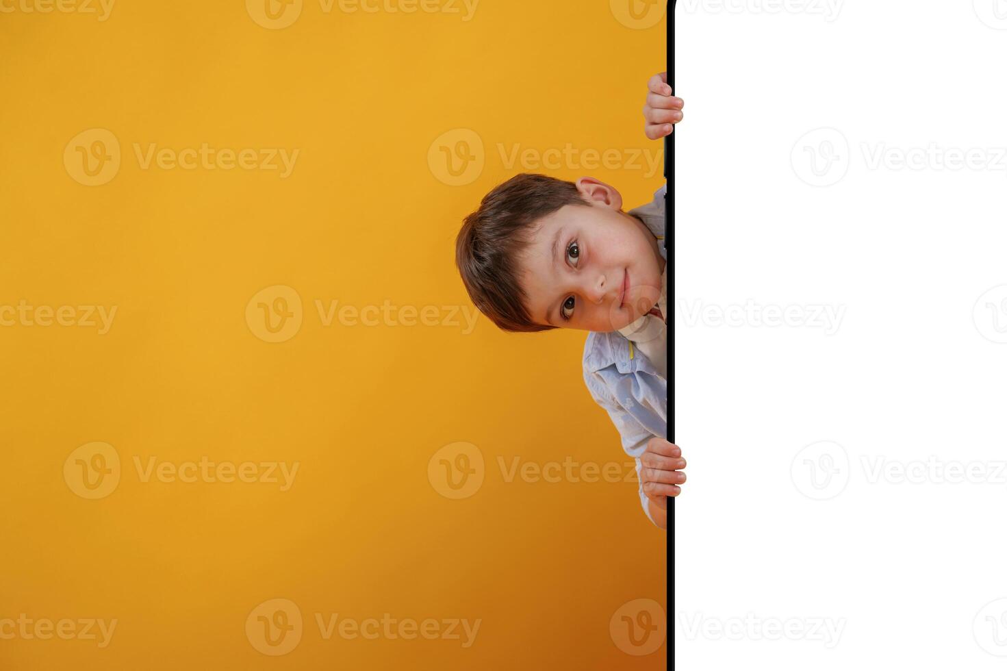 With huge smartphone, copy space ,place. Little boy is in the studio against yellow background photo