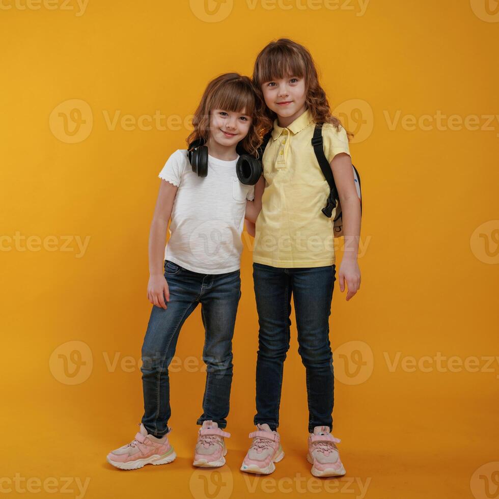 Two kids friends are standing,, embracing each other and posing against yellow background photo