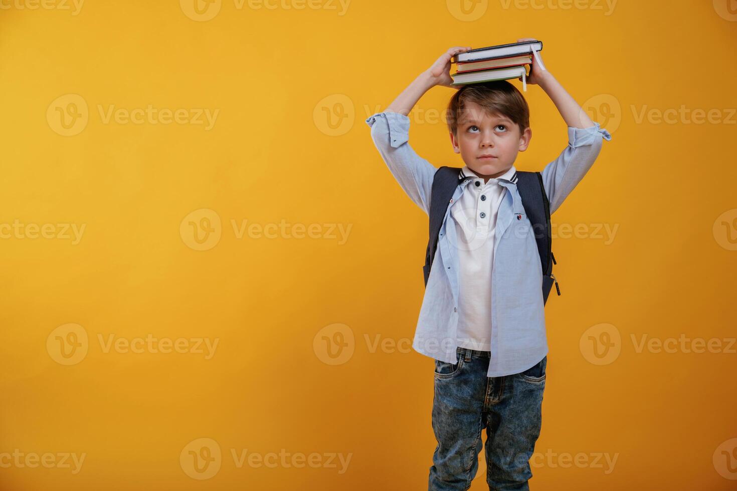 Playing ,with ,book, holding ,it on the head. Little boy is in the studio against yellow background photo