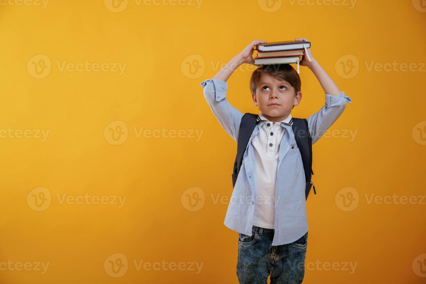 Playing ,with book, holding it on the head. Little boy is in the studio against yellow background photo