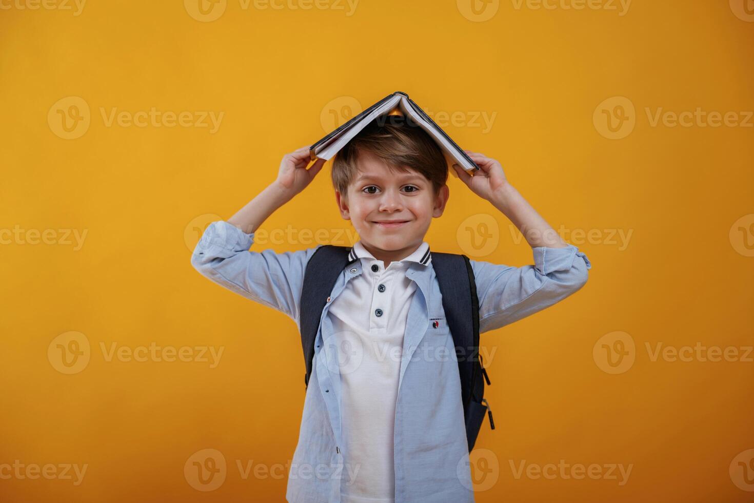 Playing, with book, holding, it on the head. Little boy is in the studio against yellow background photo