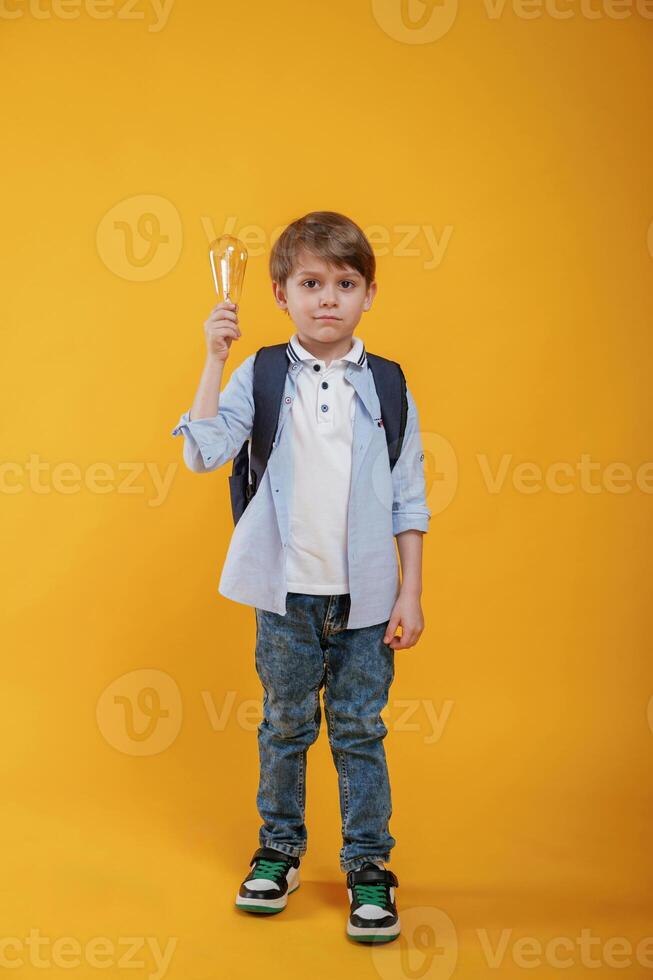 Light ,bulb in hand. Conception of smart person and idea. Little boy is in the studio against yellow background photo