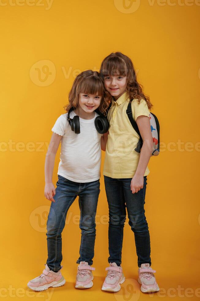 Two, kids friends are standing, embracing each other and posing against yellow background photo