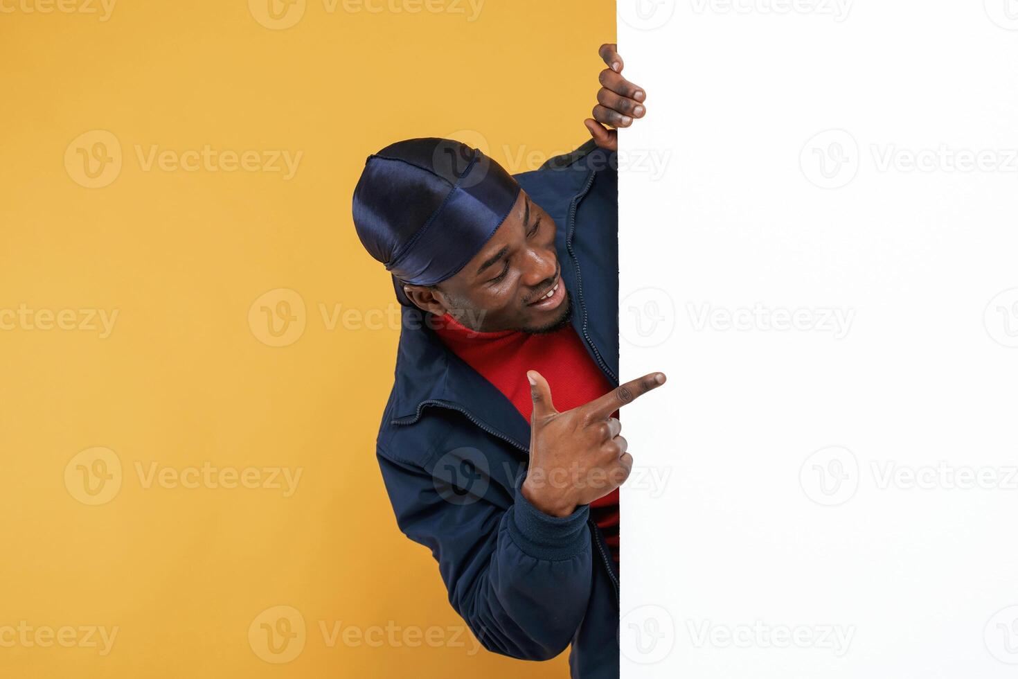 White copy space, smiling and hiding behind it. Handsome black man is in the studio against yellow background,.... photo