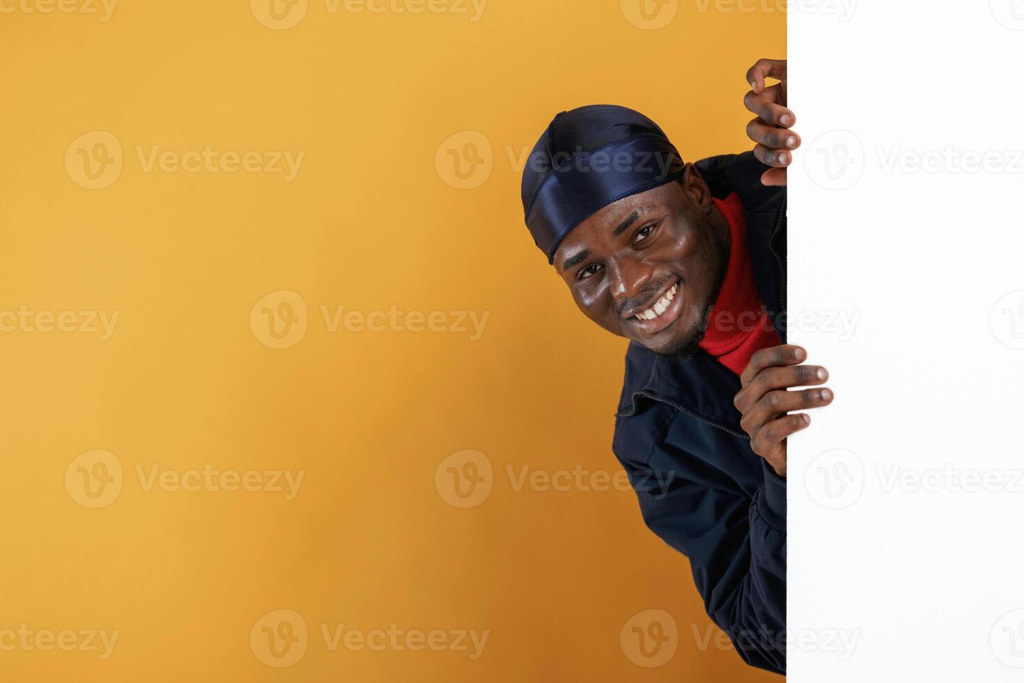 White copy space, smiling and hiding behind it. Handsome black man is in the studio against yellow background, photo