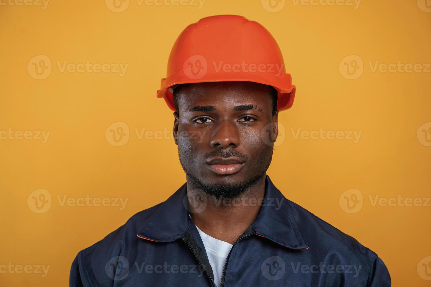 In, orange hard hat.., Construction worker. Handsome black man is in the studio against yellow background photo