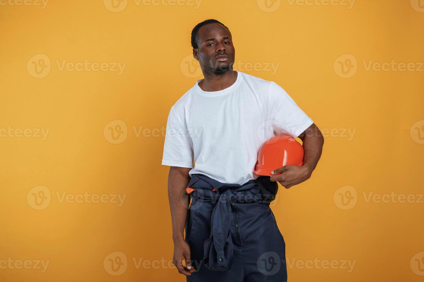 Holding hard ,hat,, in hand. Handsome black man is in the studio against yellow background photo