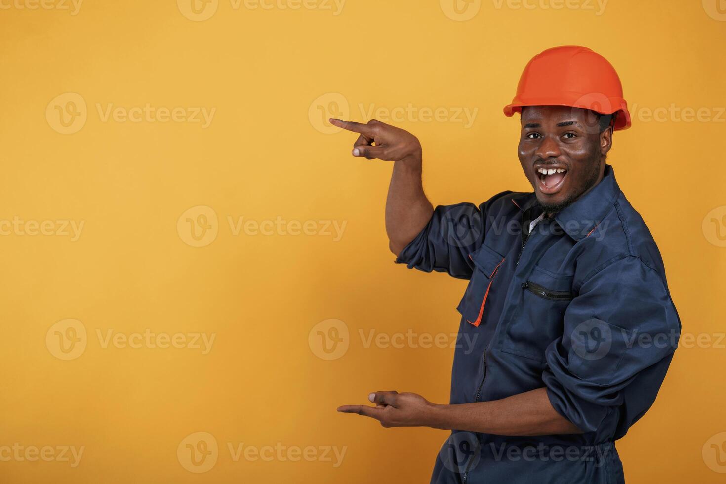 Guy in hard hat showing copy space by,, fingers. Handsome black man is in the studio against yellow background photo