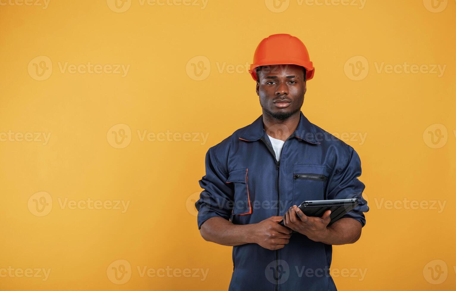 Digital, tablet in hand, construction, worker. Handsome black man is in the studio against yellow background photo