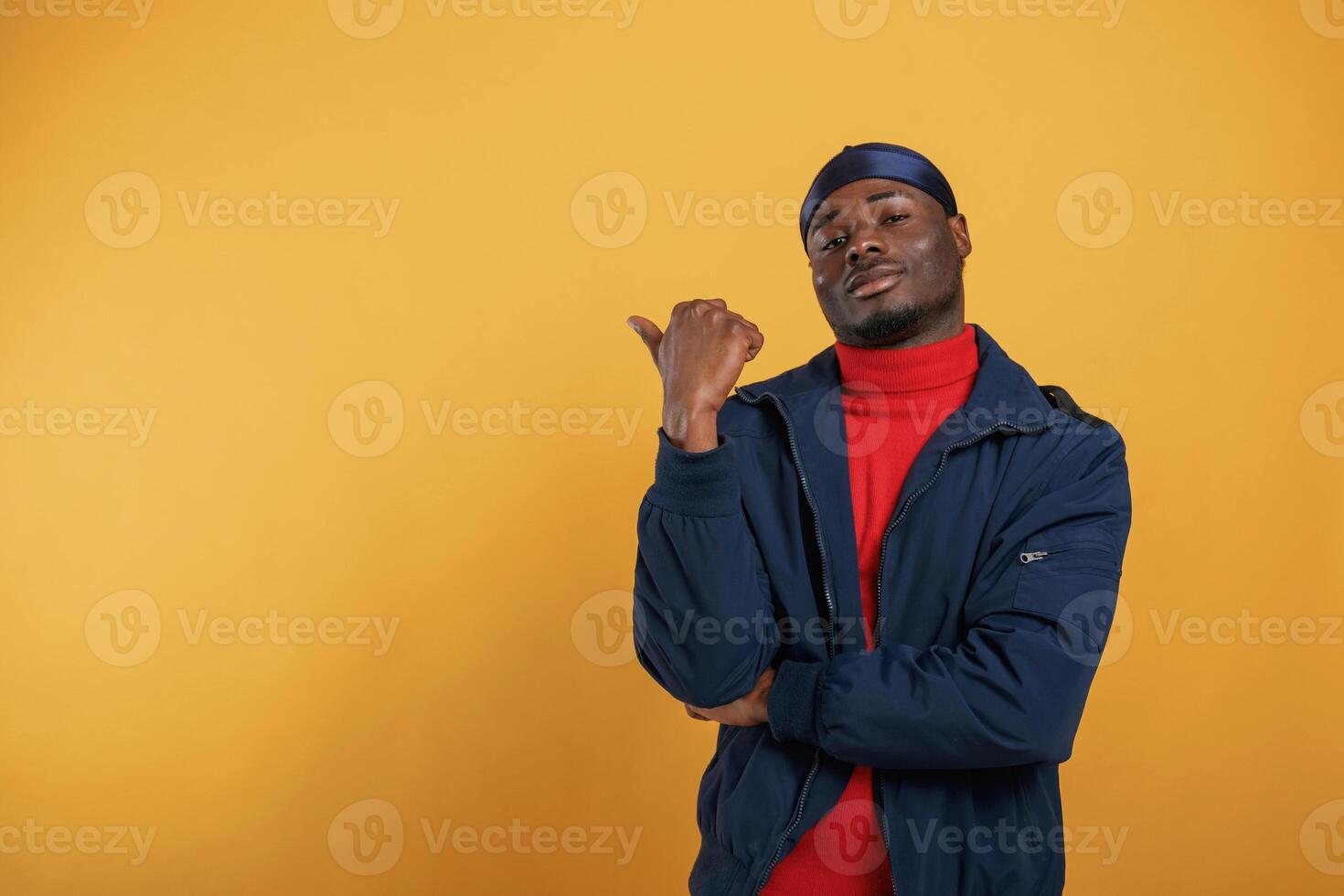 Showing something ,behind him by finger. Handsome black man is in the studio against yellow background photo