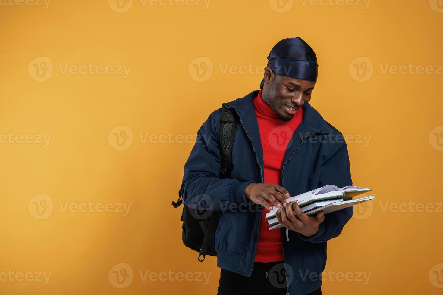Student, with books, backpack and notepad. Handsome black man is in the studio against yellow background photo