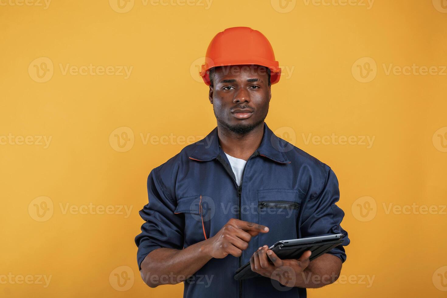 Digital tablet in hand, construction, worker. Handsome black man is in the studio against yellow background photo