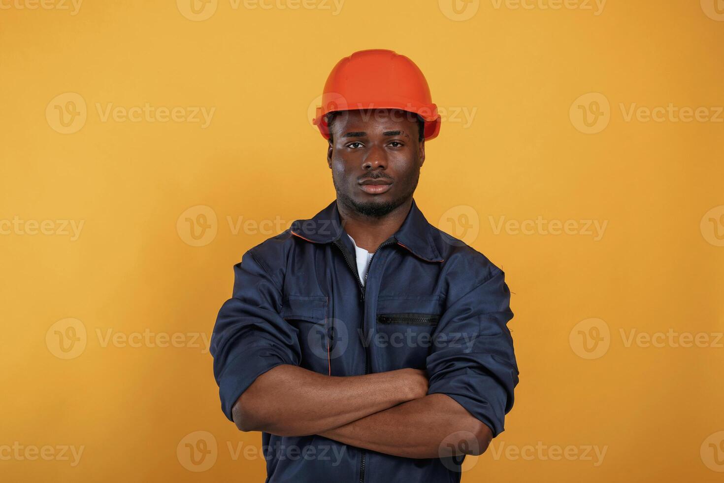 In, orange, hard hat. Construction worker. Handsome black man is in the studio against yellow background photo