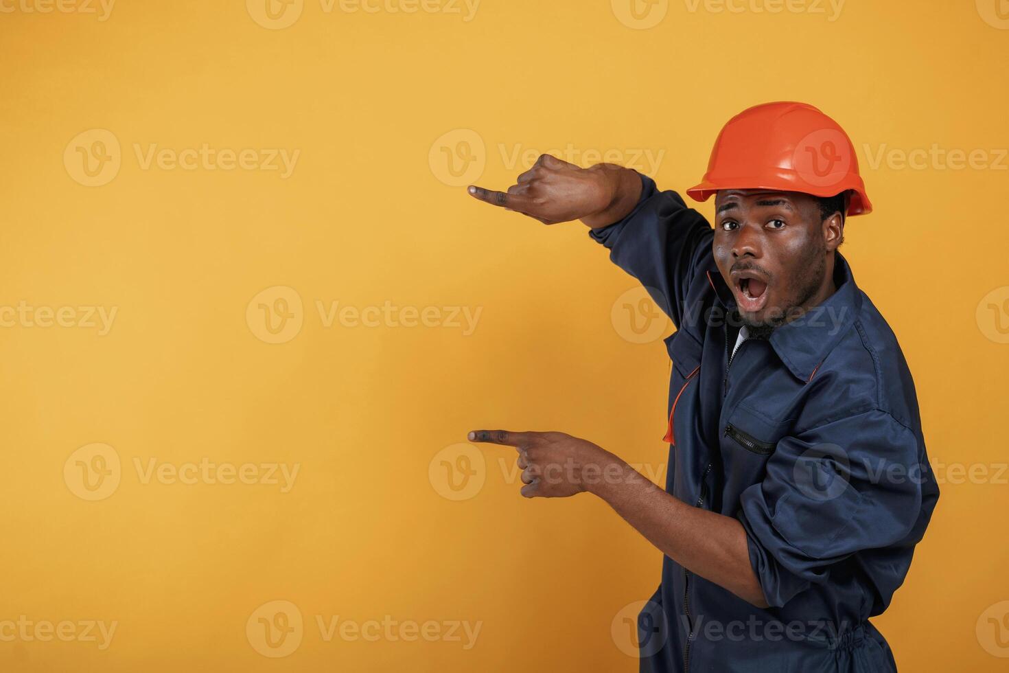 Guy in hard, hat showing copy space by fingers. Handsome black man is in the studio against yellow background photo
