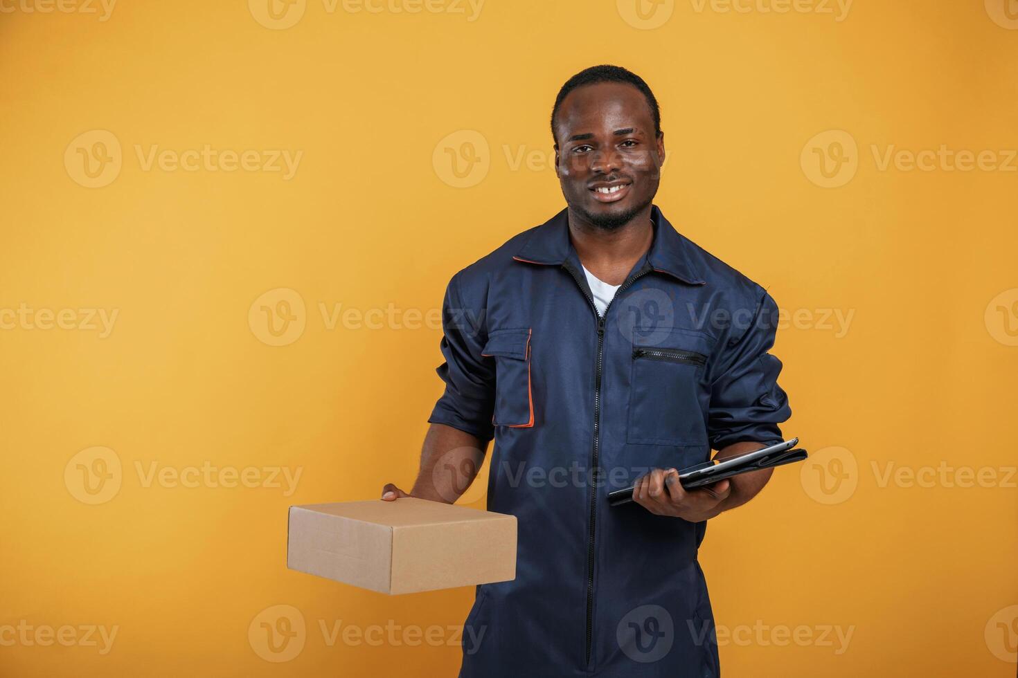Delivery, service worker with box. Handsome black man is in the studio against yellow background photo
