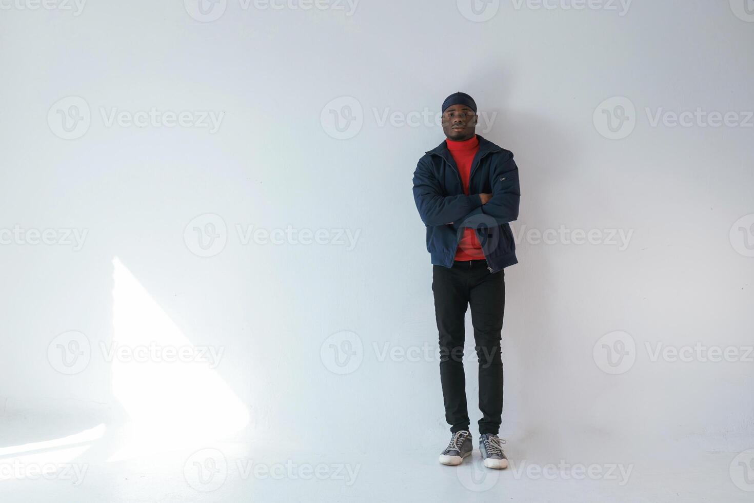 Posing with ,arms crossed. Black man in cap is in the studio against white background photo